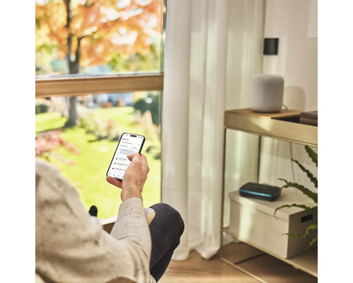 Personne avec smartphone pour contrôler l'arrosage du jardin dans le salon.