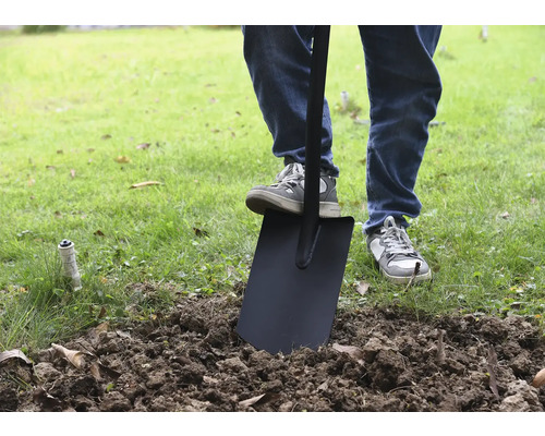 Une personne utilise une bêche dans le jardin pour retourner la terre.