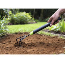 Nahaufnahme einer Hand, die eine Gartenkralle in den Boden drückt