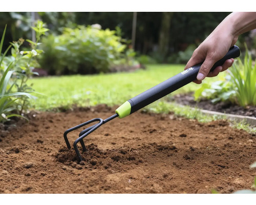 Nahaufnahme einer Hand, die eine Gartenkralle in den Boden drückt