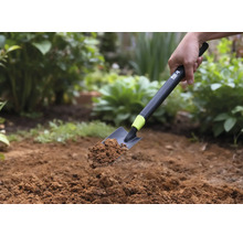 Eine Handschaufel mit Erde wird vor einem Gartenhintergrund gehalten