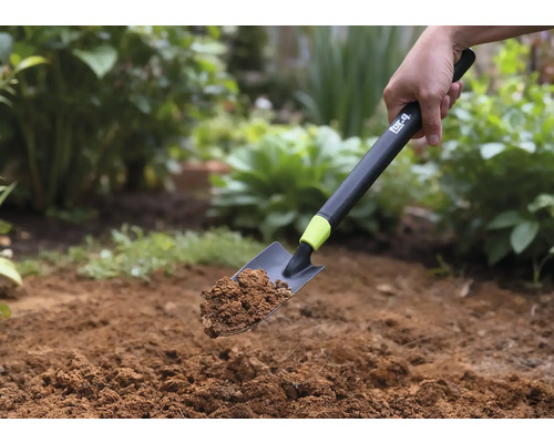 Eine Handschaufel mit Erde wird vor einem Gartenhintergrund gehalten