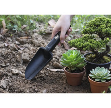 Pelle de jardin avec marquages en cours d'utilisation à côté de plantes en pot.