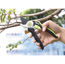 Une personne tient un sécateur de la marque for_q tout en coupant une branche.