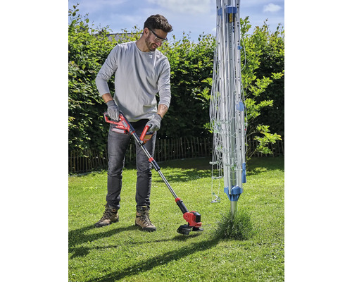 Mann schneidet Rasen mit einem Akku-Rasentrimmer im Garten neben einem Wäscheständer.