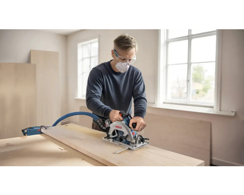 Un artisan scie une planche de bois avec une scie circulaire à main dans une pièce lumineuse