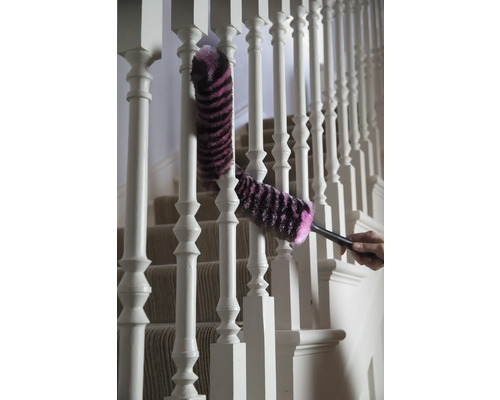 Une personne nettoie une rampe d'escalier blanche avec un plumeau.