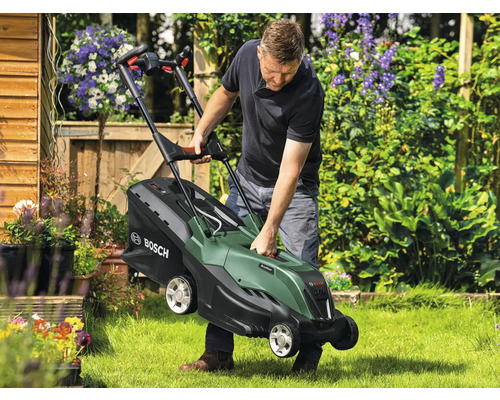 Ein Mann hebt einen Rasenmäher im Garten an
