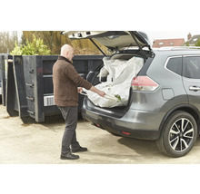 Un homme charge un big bag de déchets de jardin dans le coffre d'une voiture.