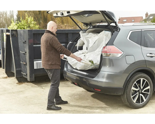 Un homme charge un big bag de déchets de jardin dans le coffre d'une voiture.