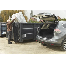 Une personne vide un sac dans un conteneur à côté d'une voiture.