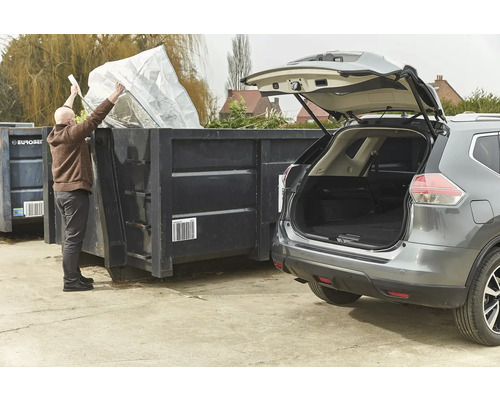 Une personne vide un sac dans un conteneur à côté d'une voiture.