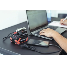 Power Bank Metabo pour charger des appareils avec un ordinateur portable et un smartphone sur une table.
