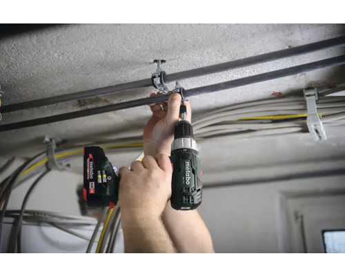 Une personne fixe un collier de serrage à un plafond à l'aide d'une visseuse sans fil.