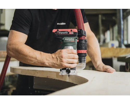 Une personne utilise une défonceuse Metabo sur une pièce, avec un tuyau d'aspiration connecté.