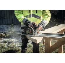 Une personne scie une planche de bois avec une scie circulaire portative Metabo et un rail de guidage.