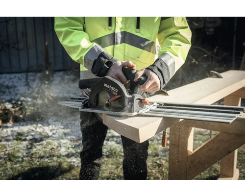 Une personne scie une planche de bois avec une scie circulaire portative Metabo et un rail de guidage.