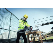 Artisan avec casque et lunettes de protection, sciant du bois avec une scie circulaire portative Metabo sur un chantier.