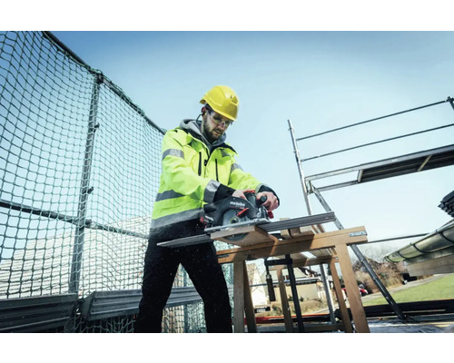 Artisan avec casque et lunettes de protection, sciant du bois avec une scie circulaire portative Metabo sur un chantier.