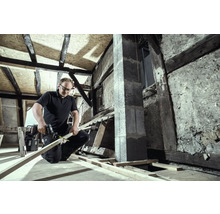 Un homme travaille avec une scie sabre sur une planche de bois dans un grenier à rénover.