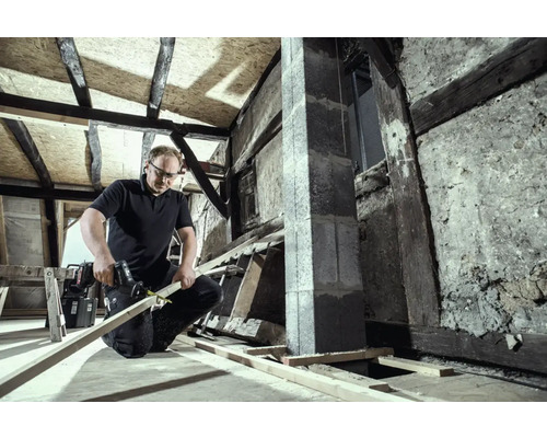 Un homme travaille avec une scie sabre sur une planche de bois dans un grenier à rénover.