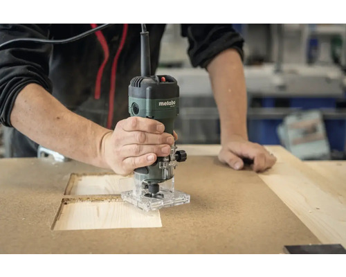 Une personne fraise une cavité dans une plaque de bois à l'aide d'une défonceuse.