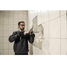 Un homme retire des carreaux du mur avec un marteau perforateur