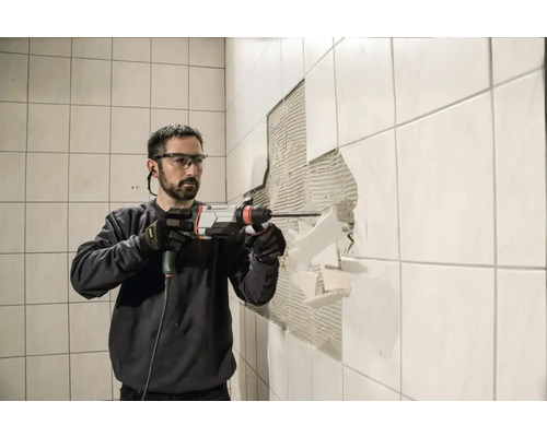 Un homme retire des carreaux du mur avec un marteau perforateur