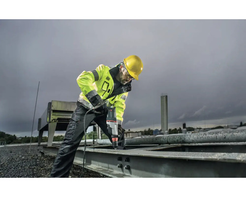 Un ouvrier du bâtiment avec un casque de protection perce une pièce métallique avec une perceuse.