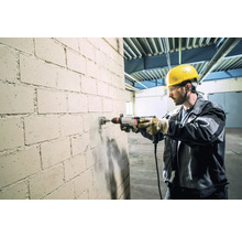 Un artisan perce un trou dans un mur de briques avec une perceuse.