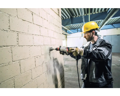 Un artisan perce un trou dans un mur de briques avec une perceuse.