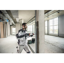 Un homme perce un mur avec un marteau perforateur dans un immeuble commercial non fini.