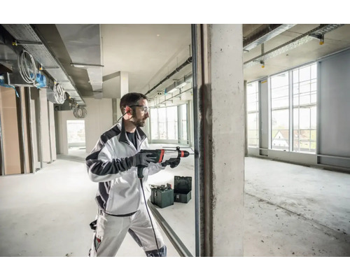 Un homme perce un mur avec un marteau perforateur dans un immeuble commercial non fini.