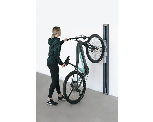 Une femme accroche un VTT électrique à un support mural.