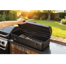 Boîte à ustensiles de barbecue ouverte avec spatule à côté du barbecue dans le jardin.