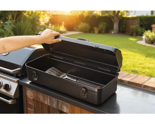 Boîte à ustensiles de barbecue ouverte avec spatule à côté du barbecue dans le jardin.