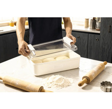 Boîte à pâte avec couvercle et deux rouleaux à pâtisserie ainsi que de la farine sur un plan de travail de cuisine