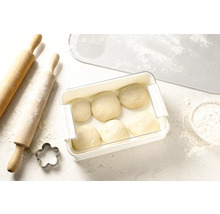 Pâte dans une boîte de conservation à côté d'un rouleau à pâtisserie, d'un emporte-pièce et d'un tapis à pâtisserie