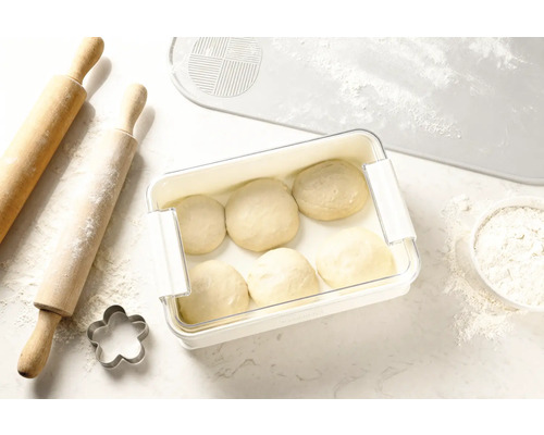 Pâte dans une boîte de conservation à côté d'un rouleau à pâtisserie, d'un emporte-pièce et d'un tapis à pâtisserie