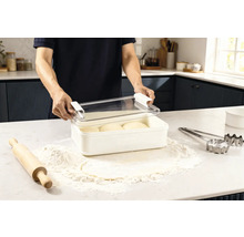 Scène dans une cuisine : un homme ouvre une boîte de conservation contenant de la pâte, entourée de farine, d’un rouleau à pâtisserie et d’emporte-pièces.