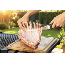 Préparation de carré d'agneau sur une planche à découper en bois avec un couteau Tenneker dans le jardin.