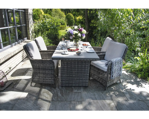 Gartenszene mit Esstisch und vier Korbsesseln mit Auflagen auf einer Steinterrasse