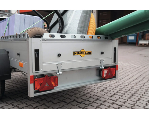 Beladener Humbaur Anhänger mit Baumaterialien wie Dämmplatten, einem Wellrohr und Rohren. Humbaur Logo auf der Heckklappe.