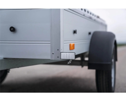 Detailansicht eines Pkw-Anhängers mit weißem Frontreflektor, gelbem Seitenreflektor und schwarzem Kunststoffkotflügel.