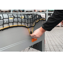 Hand befestigt ein Anhängernetz mit einer elastischen Schnur an einem Befestigungsknopf an der Bordwand eines Pkw-Anhängers.