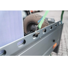 Nahaufnahme eines grünen Spanngurts mit Metallhaken, der an der Seitenreling eines Metallanhängers befestigt ist.