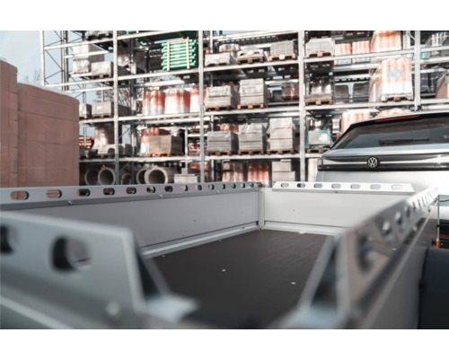 Leerer Anhänger angekoppelt an ein Auto in einem organisierten Drive In Baumarkt vor Regalen mit Baumaterialien.