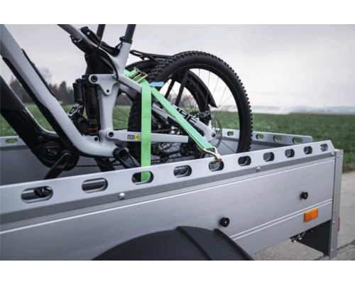 Fahrrad auf Anhänger mit einem Spanngurt gesichert.