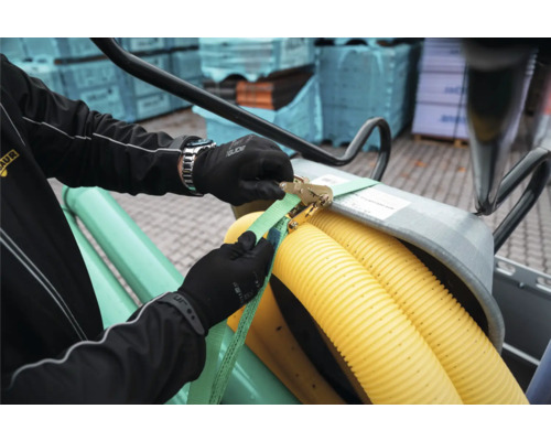 Eine Person mit Arbeitshandschuhen sichert Wellrohre aus Kunststoff mit einem Spanngurt und einer Metallratsche.