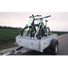 Pkw-Anhänger mit zwei Mountainbikes, die mit Spanngurten auf der Ladefläche für den Transport gesichert sind.